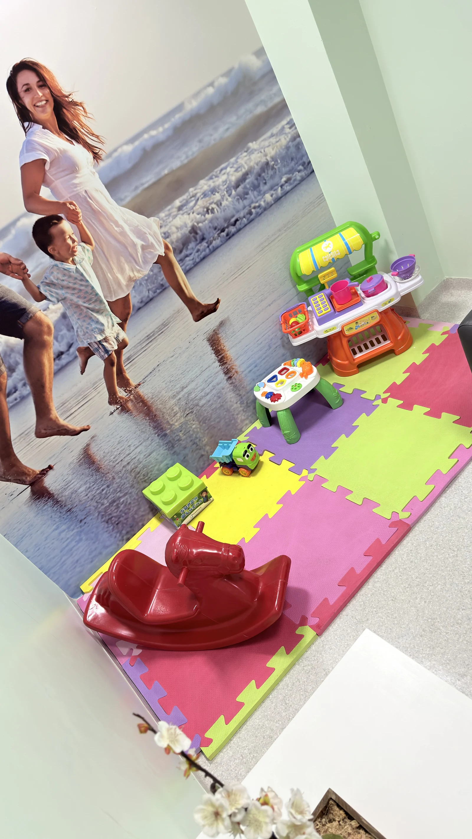 Cantinho infantil na sala de espera do setor de Oncologia do Hospital Unimed com brinquedos e mural de família na praia